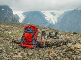 Large orange backpack with trekking poles and shoes on the background of mountains. Hiking in the highlands. Amazing bright mountain landscape of majestic nature. The time of the stop on the hike. photo