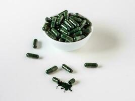 Spirulina capsules in bowl on white background. photo