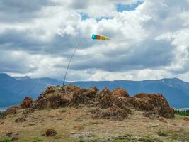 Wind sock in the mountains. Wind designator against the blue mountains. Wind sleeve flying on a blue cloudy sky. photo