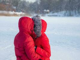 amor en el frío. un Pareja en rojo chaquetas abrazando en el nieve en invierno foto