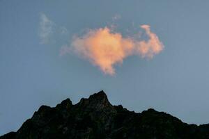 Fiery cloud in the evening over the dark silhouette of sharp mountains. Sky at sunset. Pink bright red cloud in the evening sky. photo