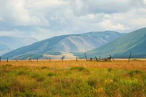 Broken wood fence along vast field in mountains in sunny day. Private pasture. Beautiful sunny alpine landscape  along field behind long fence in highlands. Vivid mountain scenery with pasture. photo