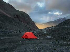 Surrealist alpine landscape with tent on rocky hill among rocks in sunrise. Beautiful morning mountains in low clouds. Surreal scenery with tent in highlands in overcast weather. photo