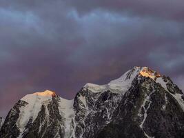 Red fiery cloud in the evening over the silhouette of sharp mountains. Top black rocks in evening golden sunshine and white-snow pointy peak. Magnificent purple sunset in the mountains. photo