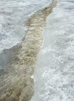 Erosion from flood waters. Spring stream. Snow washed away by a stream. Vertical view photo