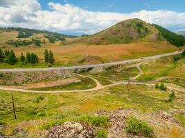 Picturesque summer mountain landscape with small bridge on the road through the pass. Turn on the asphalt mountain highway. Chuysky tract and a view of the North Chuysky Mountain range in the Altai. photo