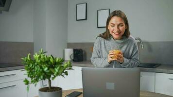 donna in piedi nel casa accogliente cucina uso il computer portatile fare libero professionista opera, chat con qualcuno, segreteria e-mail. concetto di a distanza opera video