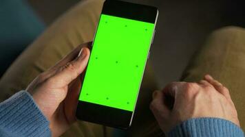man använder sig av smartphone med grön mock-up skärm i vertikal läge och dricka kaffe. man bläddring internet, tittar på innehåll, videoklipp video