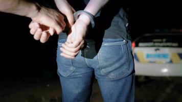 polis officer sätter handklovar på arresterad man på natt och leder honom till en polis bil video