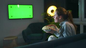 bak- se av en kvinna Sammanträde på en soffa i de levande rum i de kväll och tittar på en grön TV skärm mockup, är känslomässigt orolig handla om Vad hon ser video