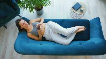 Overhead shot of relaxed woman in wireless headphones listening to music and using mobile apps on smartphone with green mock-up screen video