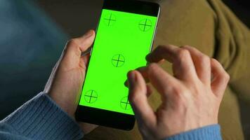 man använder sig av smartphone med grön mock-up skärm i vertikal läge och dricka kaffe. man bläddring internet, tittar på innehåll, videoklipp video