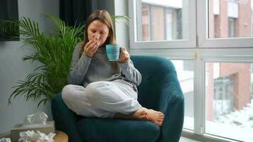 Unhealthy Caucasian woman sits in a chair and sneezes or blows her nose into a napkin because she has a cold, flu, coronavirus. It is snowing outside video