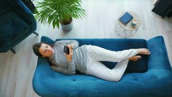 Overhead shot of relaxed woman in wireless headphones listening to music and using mobile apps on smartphone with green mock-up screen video