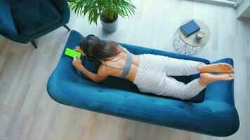 Overhead shot of relaxed woman in wireless headphones listening to music and using mobile apps on smartphone with green mock-up screen video