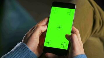 man använder sig av smartphone med grön mock-up skärm i vertikal läge och dricka kaffe. man bläddring internet, tittar på innehåll, videoklipp video