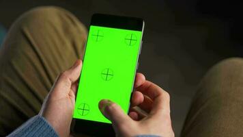 man använder sig av smartphone med grön mock-up skärm i vertikal läge och dricka kaffe. man bläddring internet, tittar på innehåll, videoklipp video
