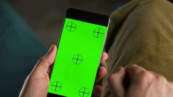 man använder sig av smartphone med grön mock-up skärm i vertikal läge och dricka kaffe. man bläddring internet, tittar på innehåll, videoklipp video