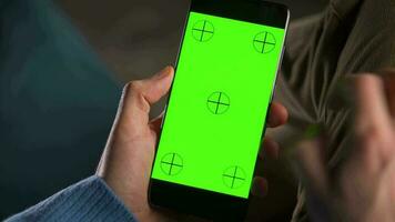 man använder sig av smartphone med grön mock-up skärm i vertikal läge och dricka kaffe. man bläddring internet, tittar på innehåll, videoklipp video