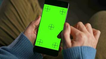 man använder sig av smartphone med grön mock-up skärm i vertikal läge och dricka kaffe. man bläddring internet, tittar på innehåll, videoklipp video