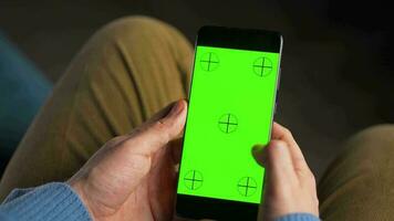 Man using smartphone with green mock-up screen in vertical mode and drinking coffee. Man browsing Internet, watching content, videos