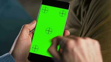 Mens gebruik makend van smartphone met groen mock-up scherm in verticaal mode en drinken koffie. Mens browsen internetten, aan het kijken inhoud, videos