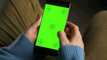 man använder sig av smartphone med grön mock-up skärm i vertikal läge och dricka kaffe. man bläddring internet, tittar på innehåll, videoklipp video