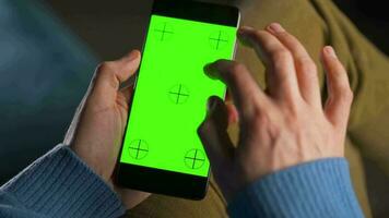 man använder sig av smartphone med grön mock-up skärm i vertikal läge och dricka kaffe. man bläddring internet, tittar på innehåll, videoklipp video