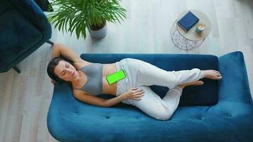 Overhead shot of relaxed woman in wireless headphones listening to music and using mobile apps on smartphone with green mock-up screen video