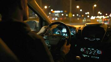 hombre conducción coche mediante el calles de noche ciudad. ver desde el espalda asiento de el coche video