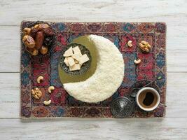 Biscuit cake sprinkled with white chocolate in the shape of a Crescent moon, served with dates and coffee cup photo