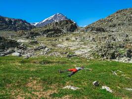 Man lying down in nature and resting. Happy male tourist after climbing lies and rests on the green grass against the background of the mountains. photo