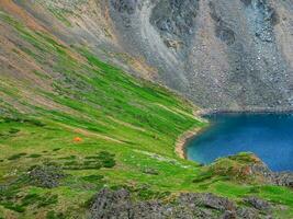 Camping on a steep green slope. Fantastic landscape of a green mountain slope with a small tent. Scenic alpine landscape with tent on green hill among rocks. Secluded camping in the mountains. photo