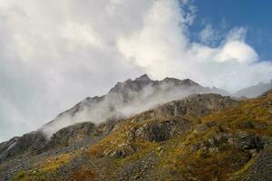 Colorful alpine landscape with rocky mountains in dance low clouds in morning sunlight.  Mountain scenery with sharp rocks among thick low clouds. Awesome view to high rockies in low cloudiness. photo