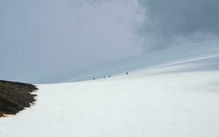 Minimalistic panoramic scenery with group climbing on large snowy mountain in sunlight under cloudy sky. Atmospheric landscape with sunshine on high snow mountain at changeable weather. photo