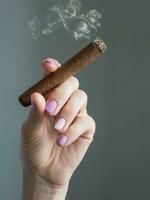 cubano cigarro en mano. un mujer mano participación un ardiente cigarro foto