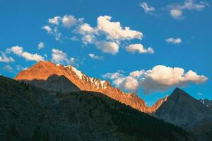 Contrasting mountains at sunset. Evening mountain landscape with rock in golden sunlight. Nature background of rocky mountain wall with sharp rock and white clouds. photo