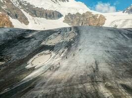 Extreme vacation in the mountains. Group of people-tourists overcome the dark dirt glacier at the mountain pass. Traveling with friends, hiking with a large company. photo