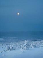 Red full cold moon over a snow-covered slope. Winter polar landscape. Cold winter weather. Harsh northern climate. Minimalistic vertical view. photo