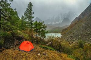 Bad weather on a hike, camping in the rain. Morning rain and fog near a mountain lake, Shavlin lake Altai, a tent camp in the fog. photo