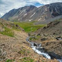 Glaciers melt, water flows into the valley. Picturesque highland landscape with mountain river in valley among high mountains with snow. Awesome alpine view to motley mountain valley, square view photo
