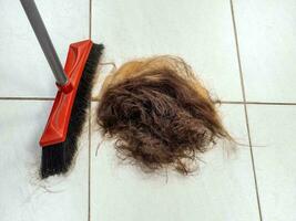 A pile of cut hair on the barber shop floor next to a broom photo
