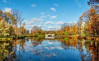 otoño parque. hermosa otoño paisaje con antiguo Roca puente, rojo arboles y reflexión en el lago. Alejandro parque, zarskoe solo Rusia foto