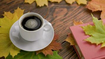 coffe cup on wooden table with book and colorful autumnal maple leaves with spinning coffee bubbles video