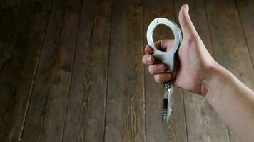 bare caucasian hand holding silver steel handcuffs on wooden board background video