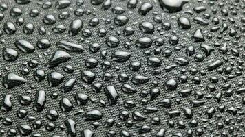 spinning closeup background of black hydrophobic fabric covered with water drops video