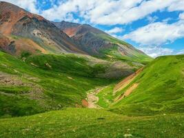 Scenic green blue alpine landscape with highland valley in sunlight and big glacier under blue cloudy sky. Shadow of clouds on green mountain valley photo