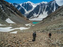 Tired climbers descend a steep mountain slope with loose stones. Group of hikers in the mountains. Travel lifestyle, hiking hard track, adventure concept in summer vacation. photo