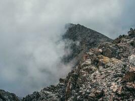 Mountain view from cliff at high altitude. Mystical landscape with beautiful sharp rocks near precipice and couloirs in low clouds. Beautiful mountain foggy scenery on abyss edge with sharp stones. photo