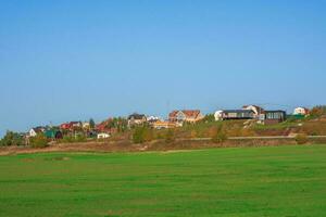 Country life. A green spring field in front of a modern village on a hill against a clear blue sky. Agricultural land. photo